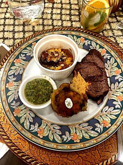 Sliced steak with chimichurri and small sides on a floral plate.